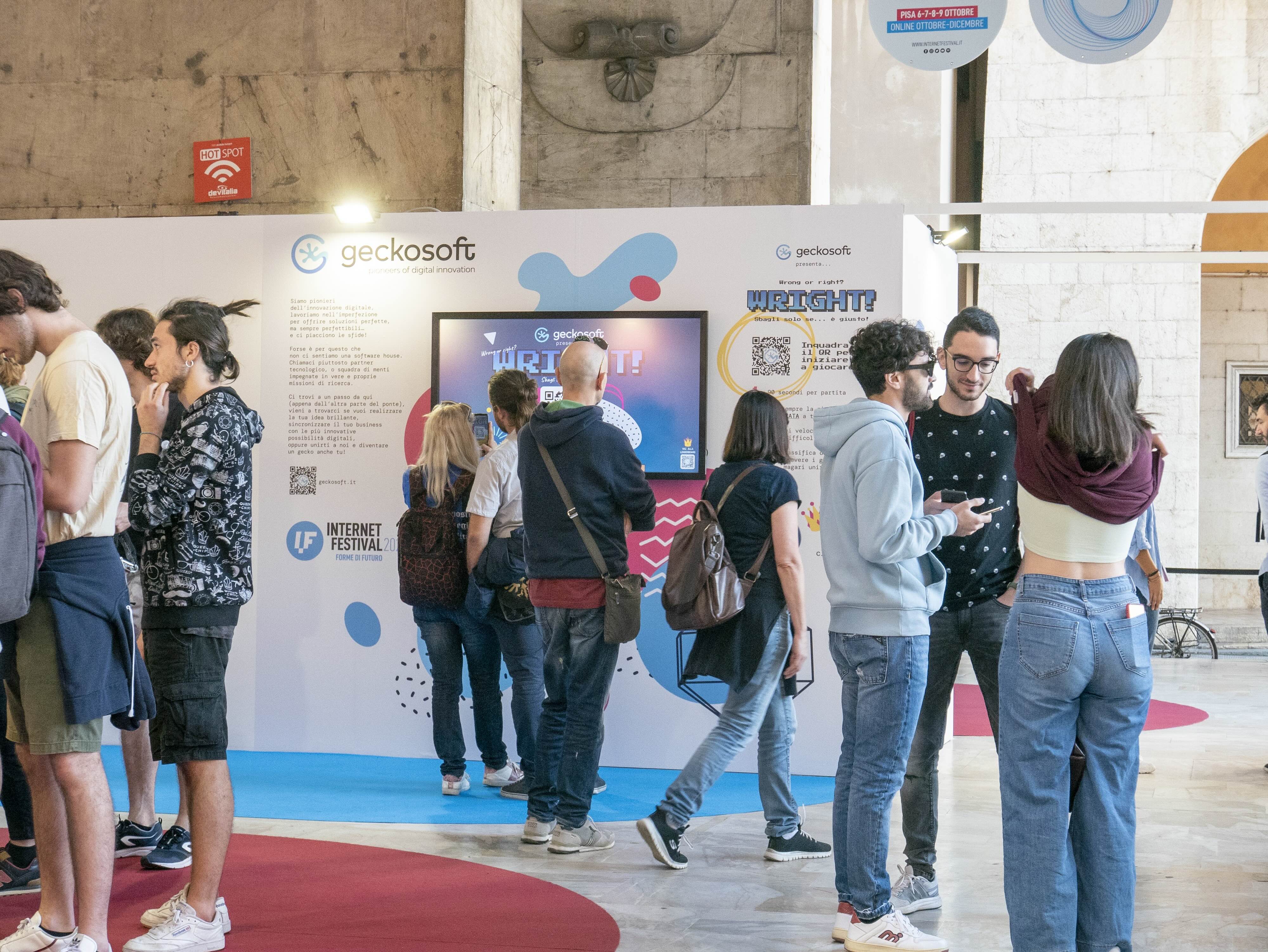 Un gruppo di persone che camminano sotto le Logge dei Banchi di Pisa durante l'Internet Festival 2022. Alcune sono davanti a uno schermo interattivo e giocanao con l'app WRIGHT! realizzata da Geckosoft